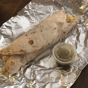 a burrito wrapped in foil with a side of salsa
