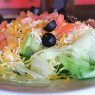 a salad with lettuce, tomatoes, black olives and cheese