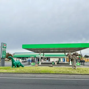 a dinosaur statue in front of a gas station