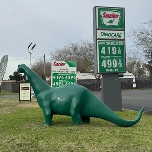 a green dinosaur in front of a gas station