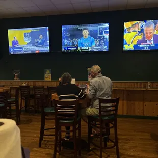 a man and a woman sitting at a table watching tvs
