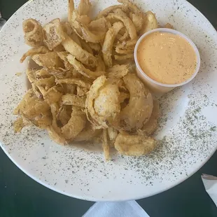 a white plate with fried onion rings and dipping sauce