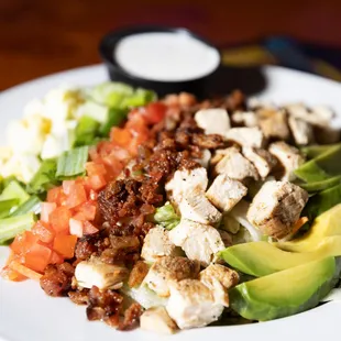 a salad with chicken, lettuce, tomatoes, avocado, bacon,