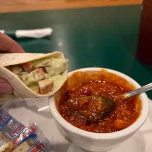 a hand holding a pita and a bowl of chili