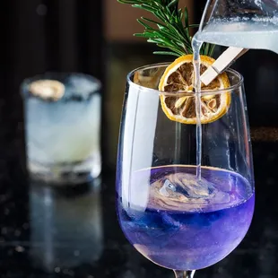 a glass of blue liquid with a sprig of rosemary