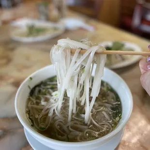 a person holding chopsticks over a bowl of noodles