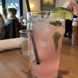 a close up of a pink drink with a lime garnish