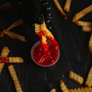 a person in black gloves dipping ketchup into a bowl of french fries