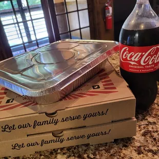 On a counter, a Coke bottle is placed beside two Genova's To Go pizza boxes, perfect for a fun meal with friends.