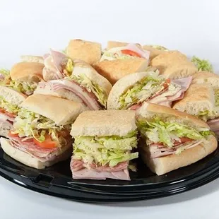 Ham and cheese sandwiches on a black plate, served on a sub tray from Genova&apos;s To Go. Delicious lunch option!