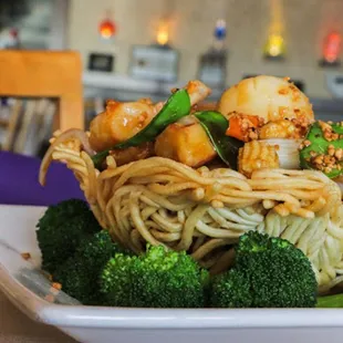 a plate of noodles with scallops and broccoli