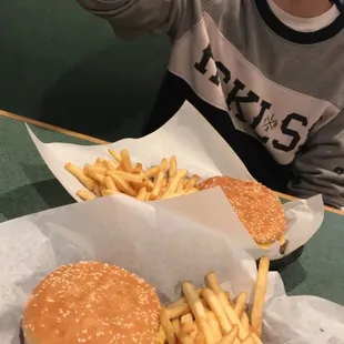 a boy sitting at a table with a hamburger and fries