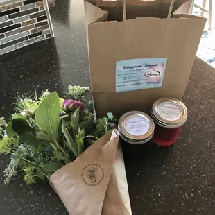 a grocery bag, two jars of jam, and a bouquet of flowers
