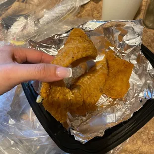 a hand holding a piece of fried chicken