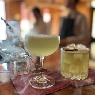 two cocktails on a table with smoke coming out of them