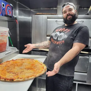 a man in a kitchen with a large pizza