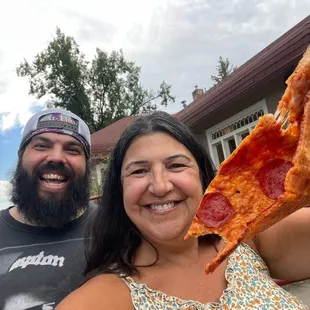 a man and a woman holding up a slice of pizza