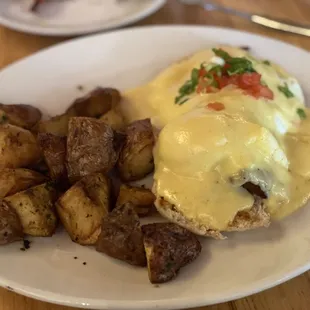 a plate of eggs benedict and potatoes