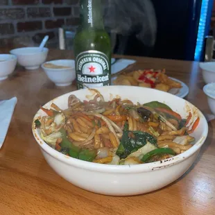 a bowl of stir fried vegetables and a bottle of beer