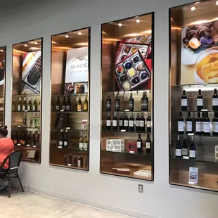 a couple sitting at a table in front of a wall of wine bottles
