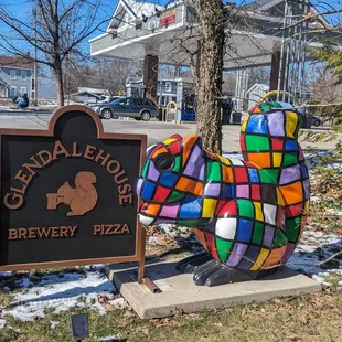 a colorful chicken statue in front of a sign