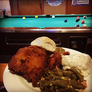 a plate of fried chicken, mashed potatoes, green beans, and mashed potatoes with a pool table in the