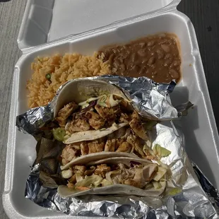 a takeout container with rice, beans, and chicken