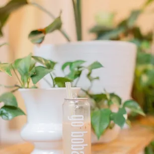 a glass of boba milk on a table with a plant in the background