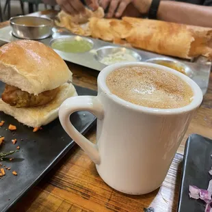 Madras Filter Coffee in the foreground, Masala Dosa in the back, Vada Pav to the side .