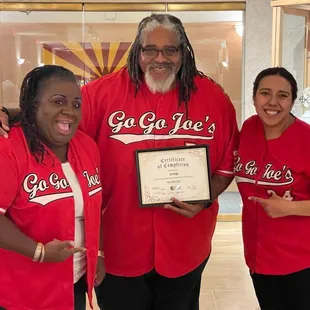 three people in red shirts holding a plaque