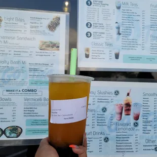 a person holding a drink in front of a menu