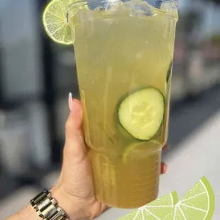 a person holding a drink with a slice of cucumber