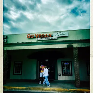 two people walking in front of a go vegan grill