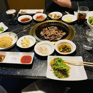 Brisket on the grill, raw pork belly, dipping sauces, dumplings, side dishes, salad.