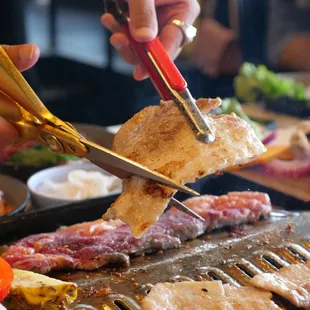 a person cutting meat on a grill