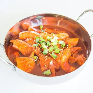 Dukbokki - spicy rice cakes in a spicy pepper sauce, fish cake, green onions, sesame leaf, onions.