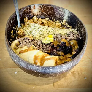 Almond butter açaí bowl in a coconut shell bowl with fair trade acai, banana, blueberries, almond butter, cacao nibs &amp; granola