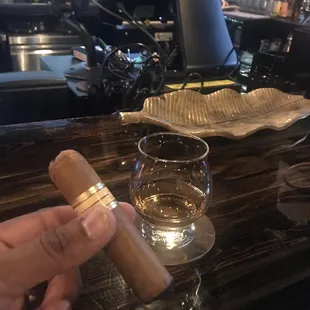 a hand holding a cigar and a glass of whiskey