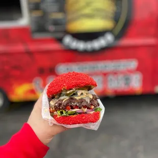 a person holding a hamburger in front of a food truck