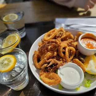 a plate of onion rings and dipping sauces