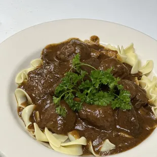 Hungarian Goulash  tender chunks of beef in brown sauce, served over egg wide noodles with homemade soup or salad.