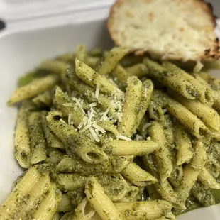 Pinnae pesto pasta garlic cheesy bread. Parmesan cheese on top.