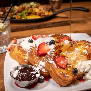 a plate of french toast with strawberries, blueberries, and whipped cream