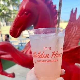 a person holding a drink in front of a horse statue