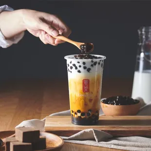 a person holding a spoon over a cup of bubble tea