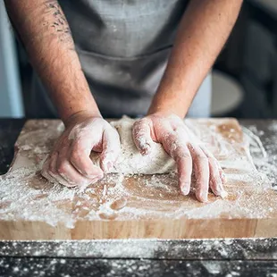 a person kneading dough on a cutting board