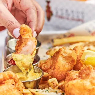 a hand dipping a piece of fried shrimp