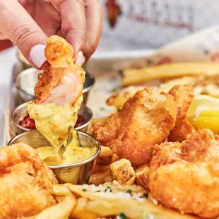 a person dipping a piece of fried shrimp