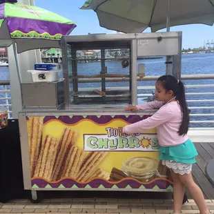 a little girl standing in front of a food cart