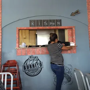 Servers pick up orders INSIDE kitchen window, decorated with Periodic Table of Elements spelling out "Kitchen". Nerdy cute.